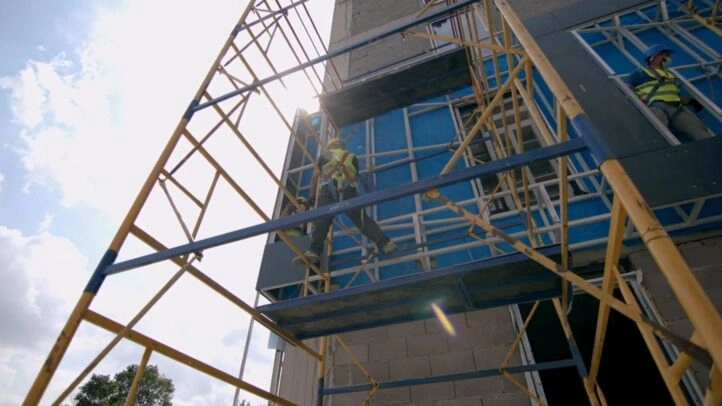 Construction workers wearing safety harnesses while working on high-rise scaffolding.