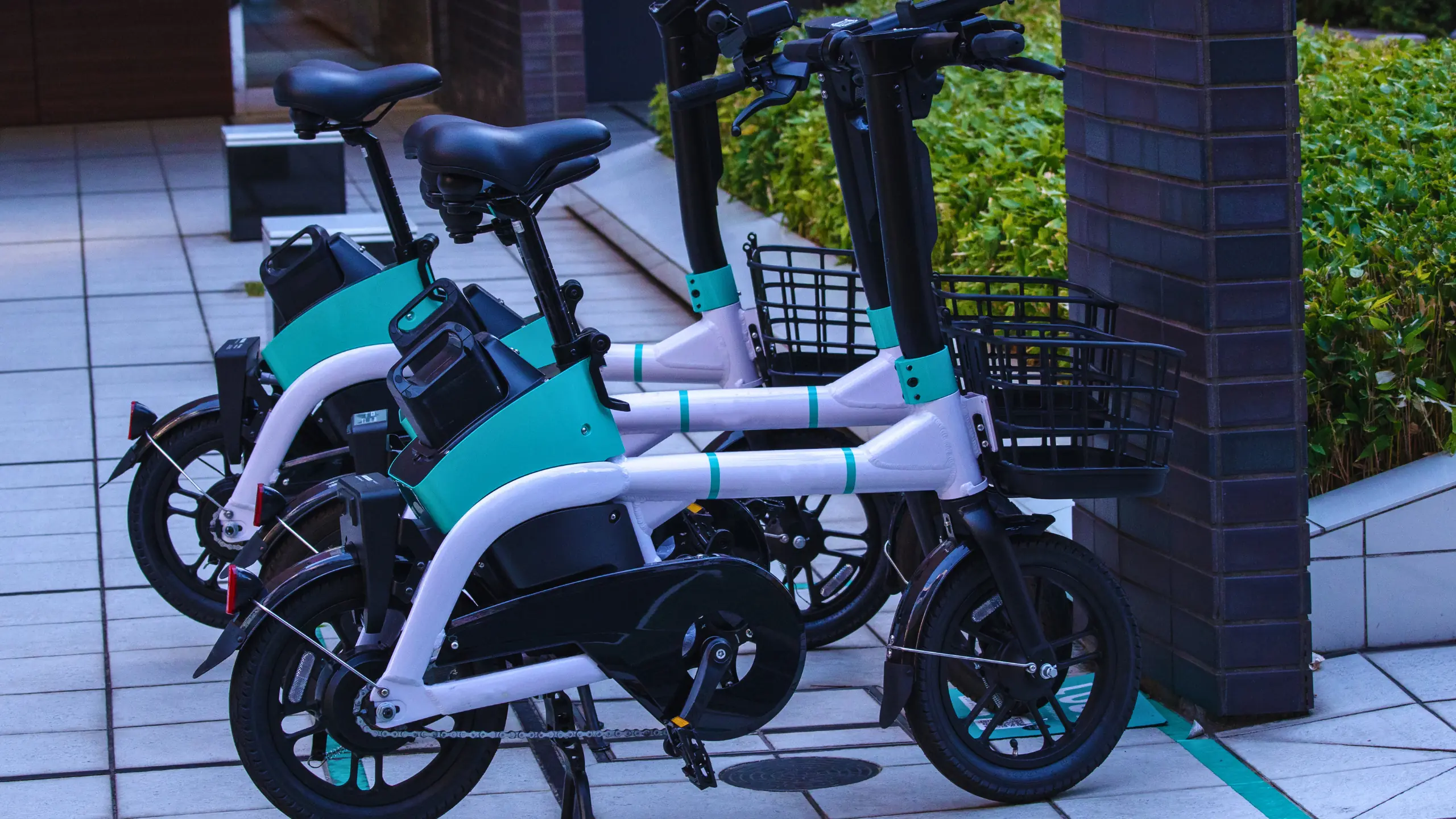 A row of green electric scooters lined up on a city sidewalk beside a busy street.