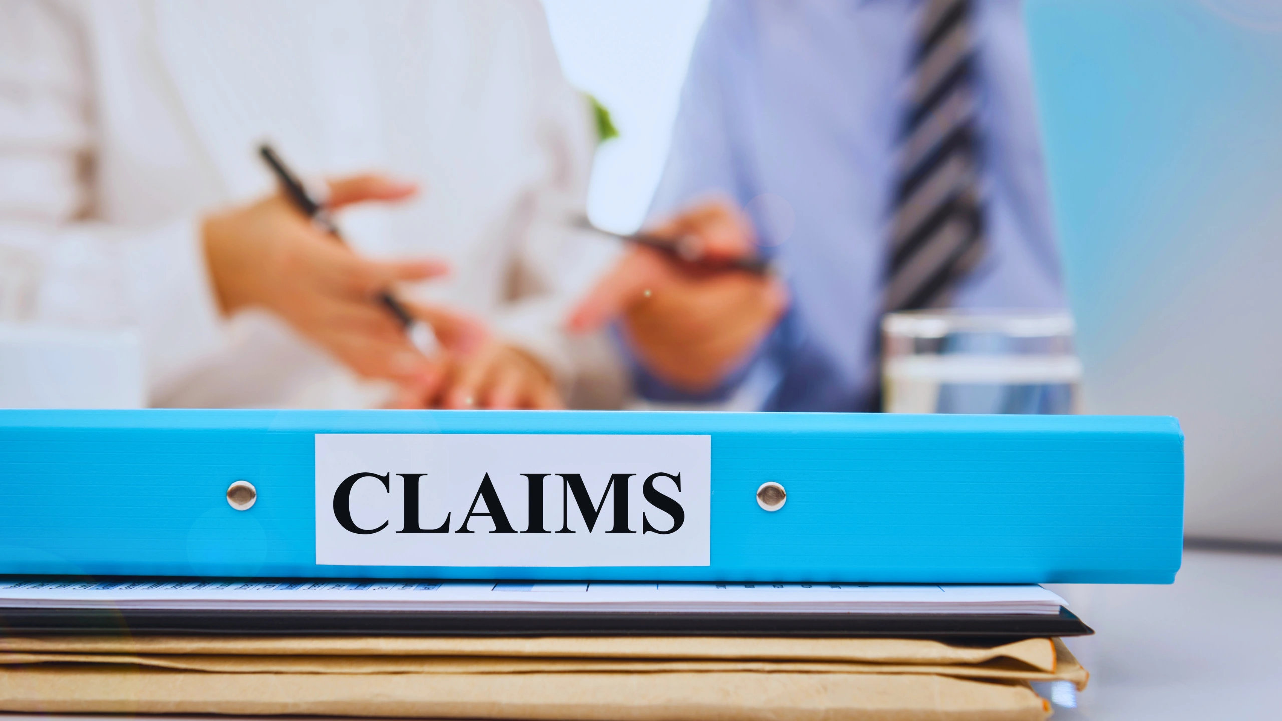 Clarity On ERISA Liens 1 A blue binder labeled "CLAIMS" sitting on a desk with professionals in the background.