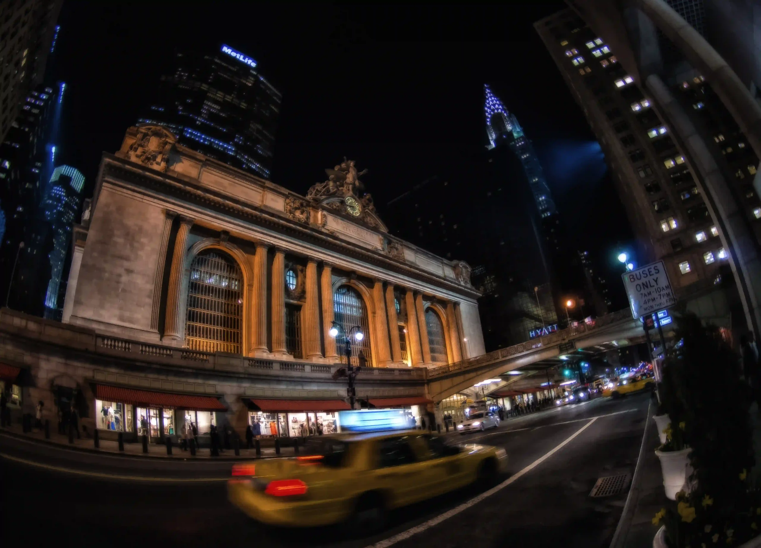 Historic building at night with blurred yellow taxi passing by.