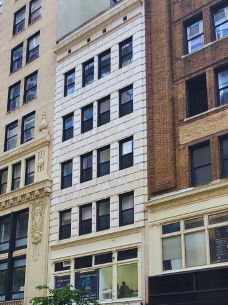 A white brick apartment building nestled between two taller brownstone city buildings.