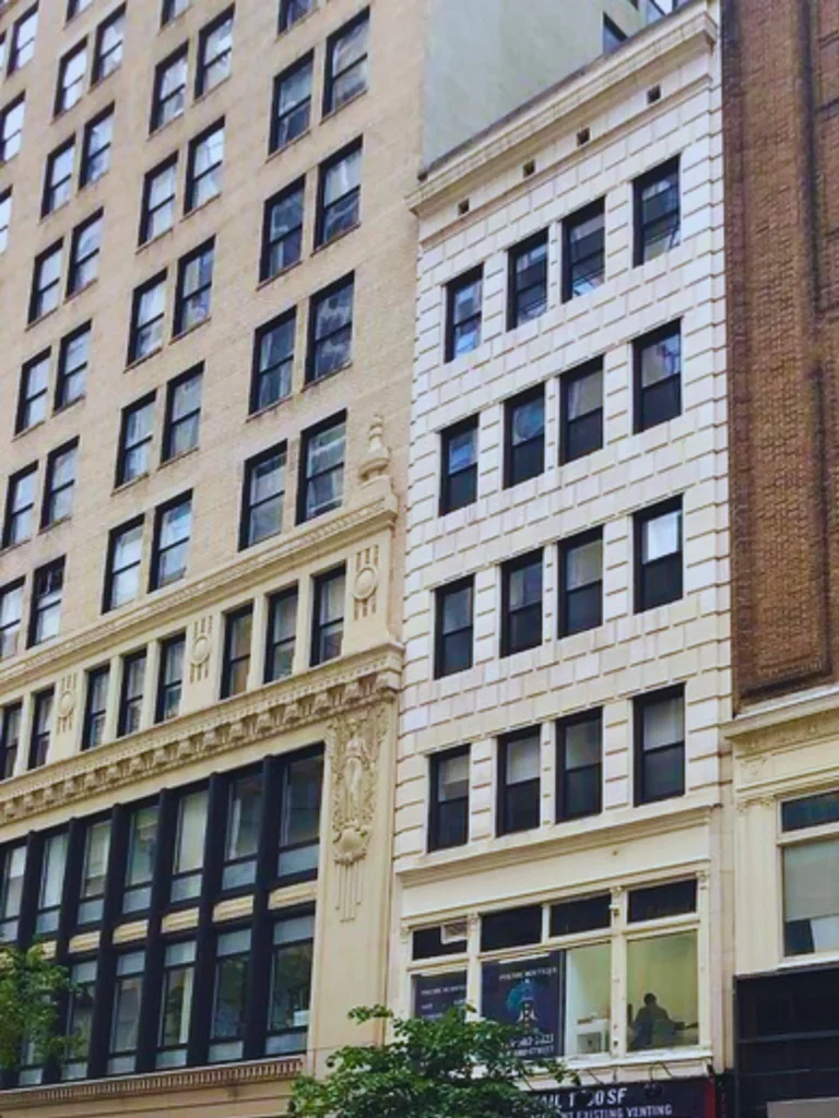 A white brick apartment building nestled between two taller brownstone city buildings.
