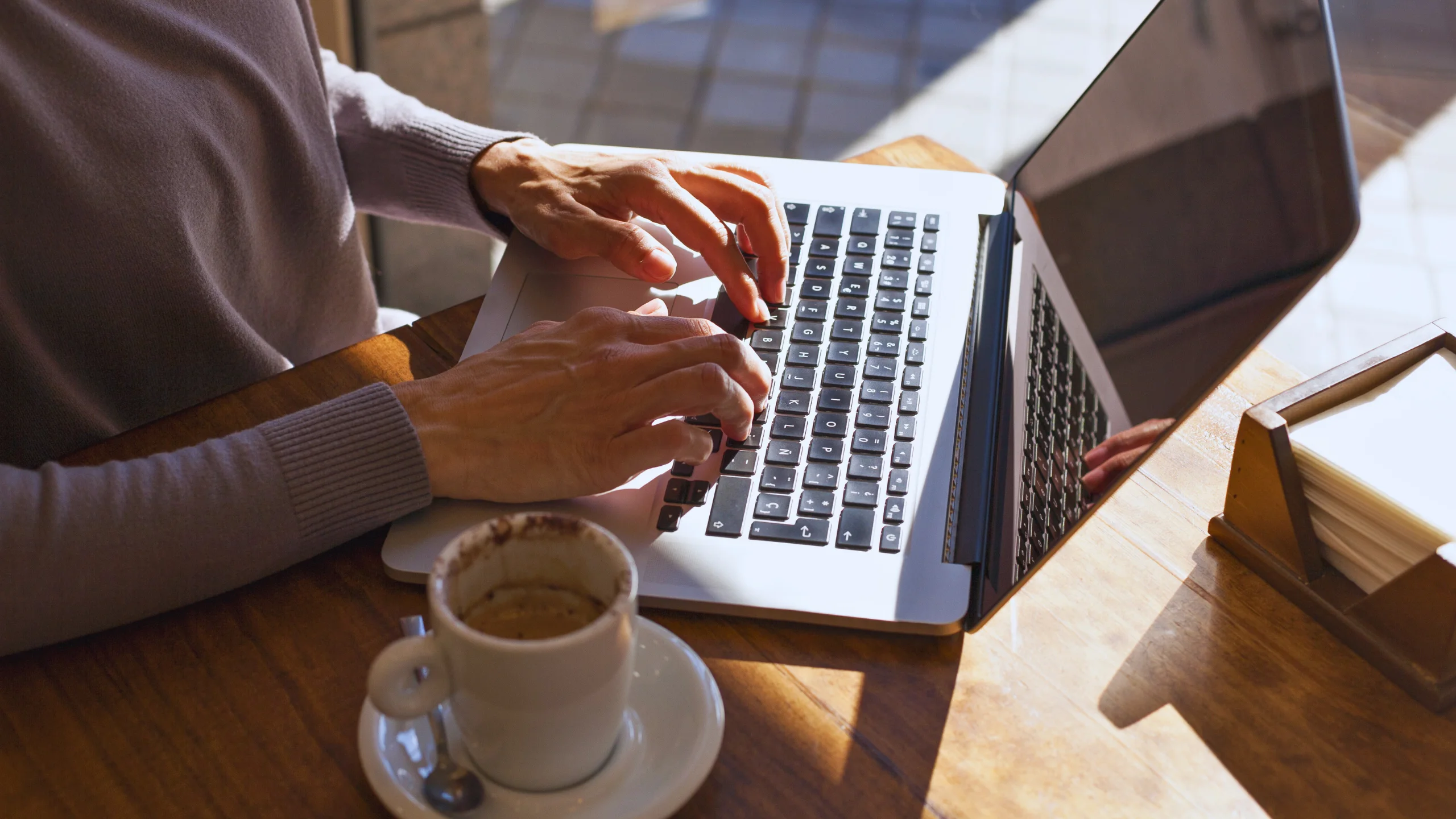 Person typing on laptop next to espresso cup.