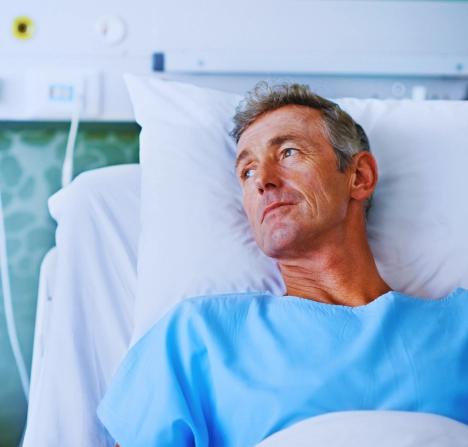 A person lying in a hospital bed wearing a light blue hospital gown.