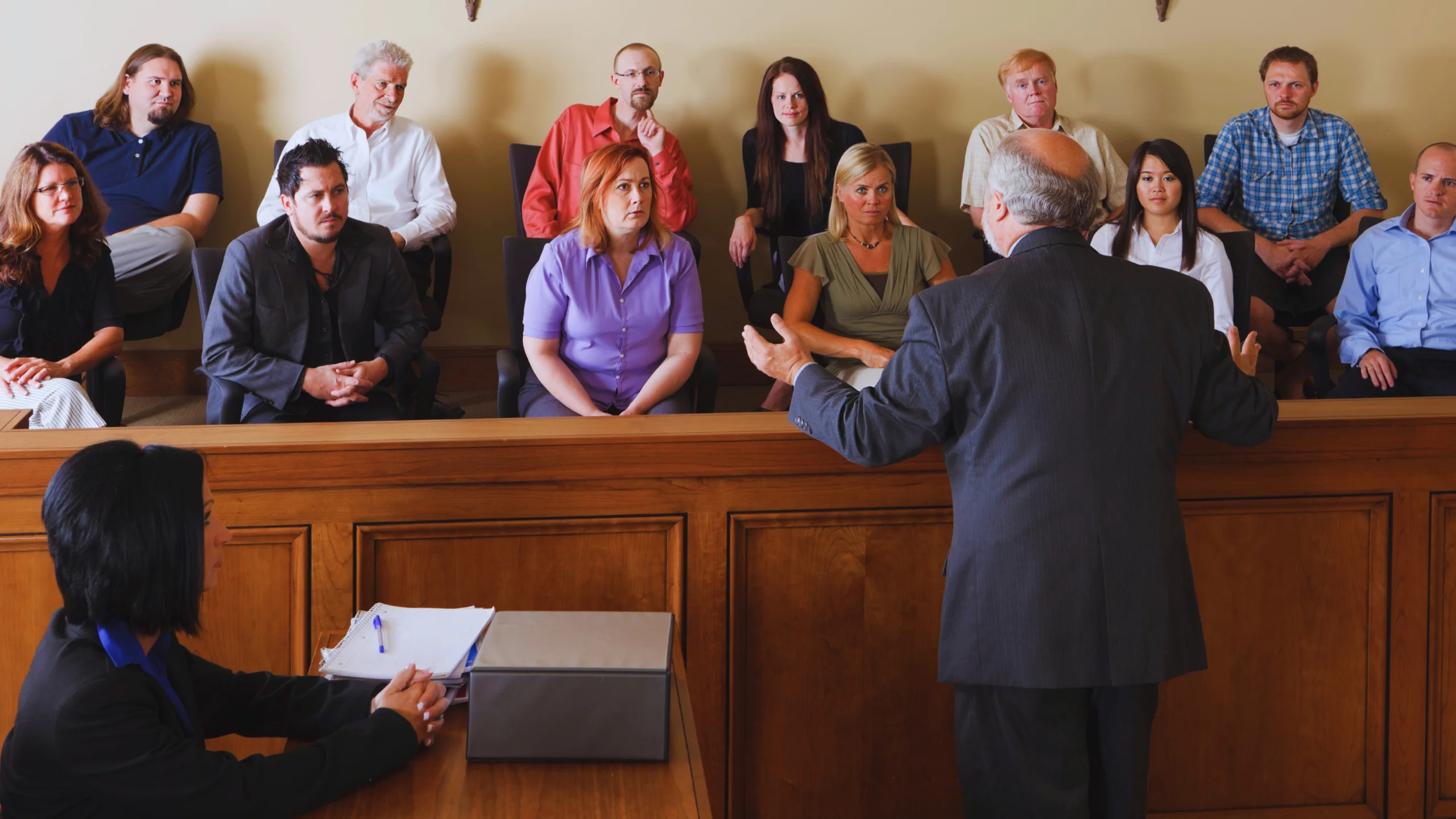 A lawyer in a suit addresses a diverse jury in a courtroom.