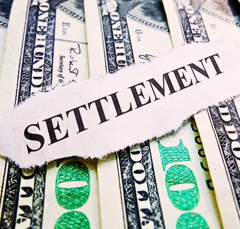 he word "SETTLEMENT" printed on a torn piece of paper placed over several U.S. hundred-dollar bills.