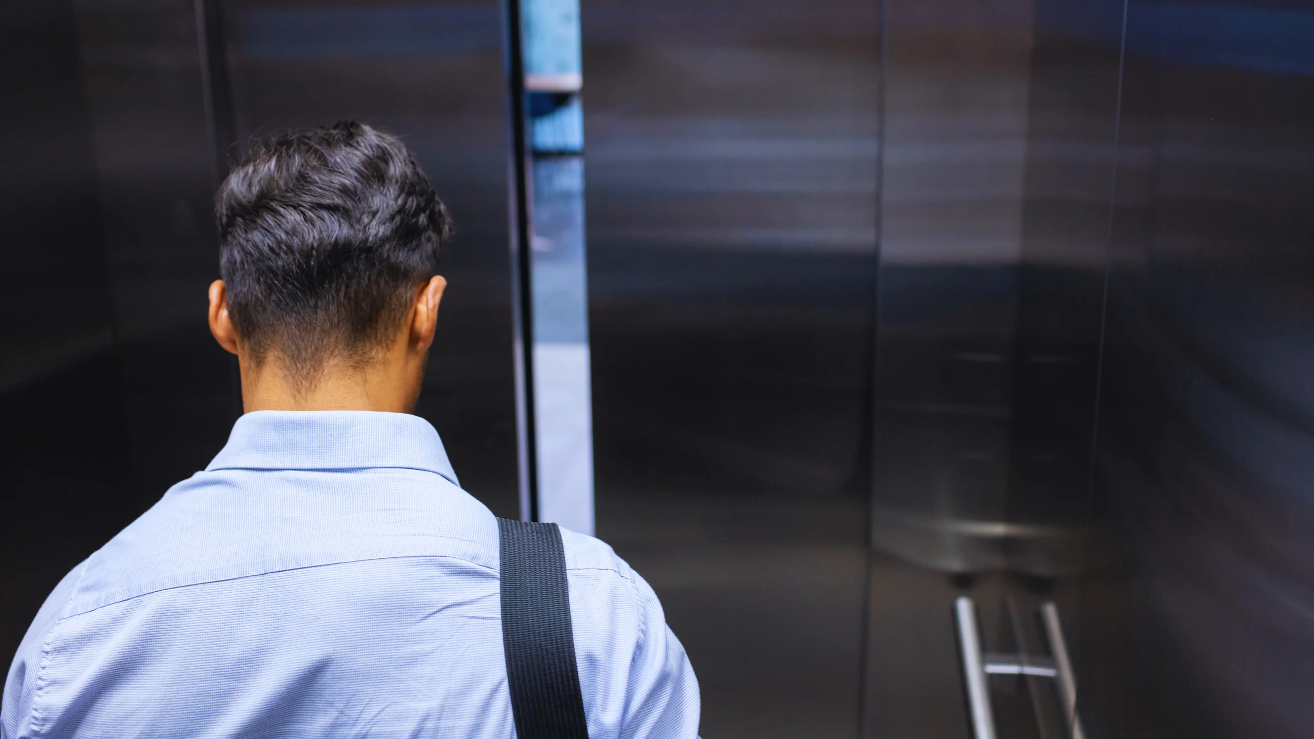 Man in a blue shirt standing inside a modern elevator with metallic doors.