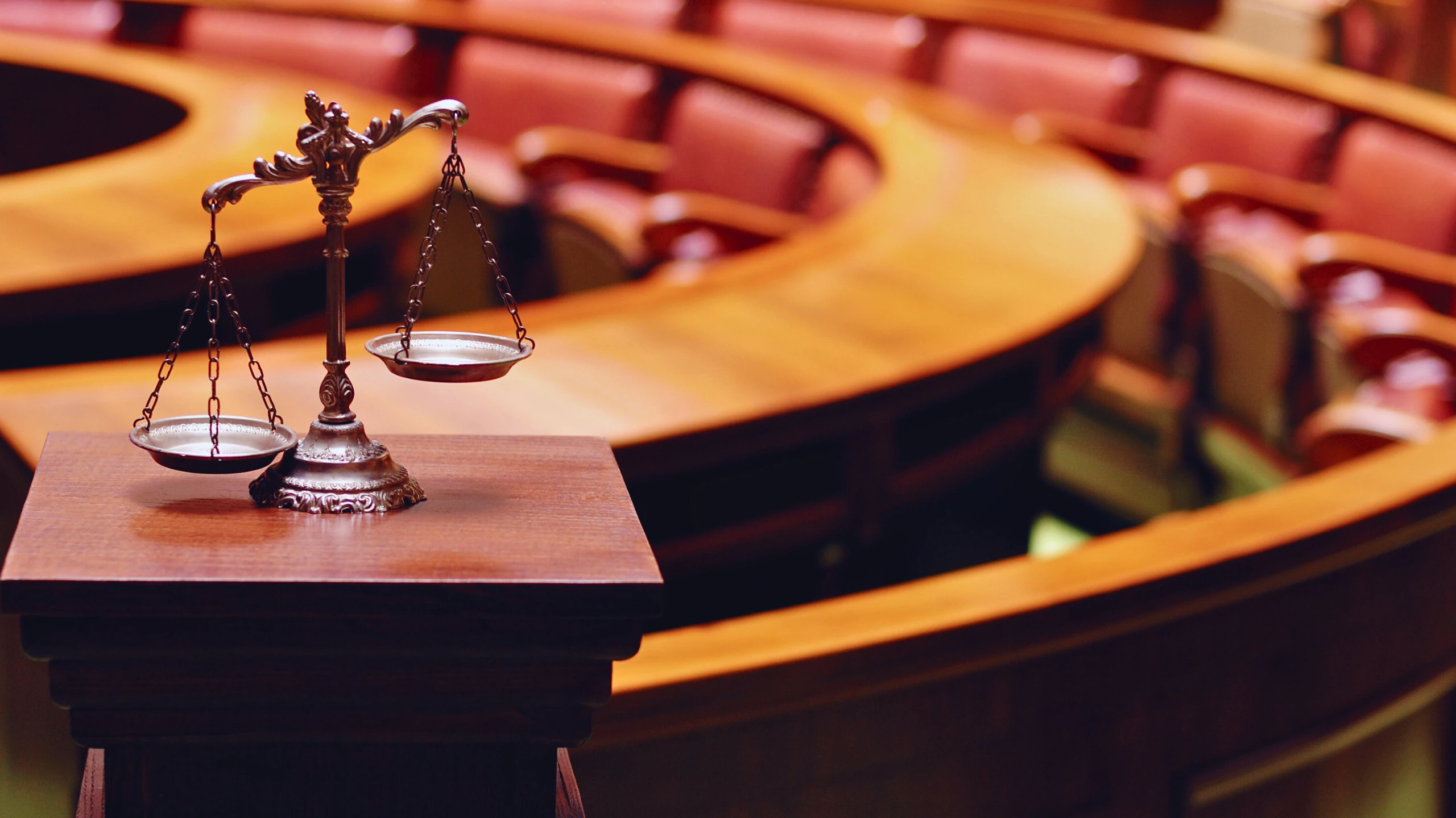 The Case For More Transparency In Grand Jury Proceedings 1 An empty courtroom with wooden benches, a judge’s bench, a microphone, and scales of justice at the front.