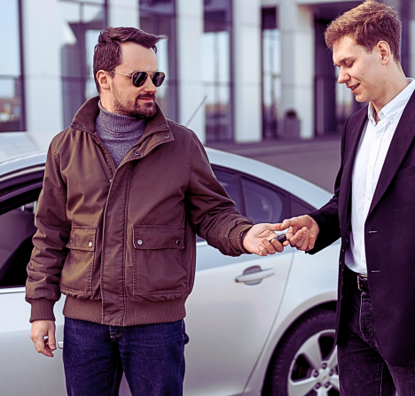 two men standing outside a modern building near a silver car.