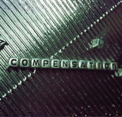 the word "COMPENSATION" spelled out with small letter blocks on a textured metallic surface.
